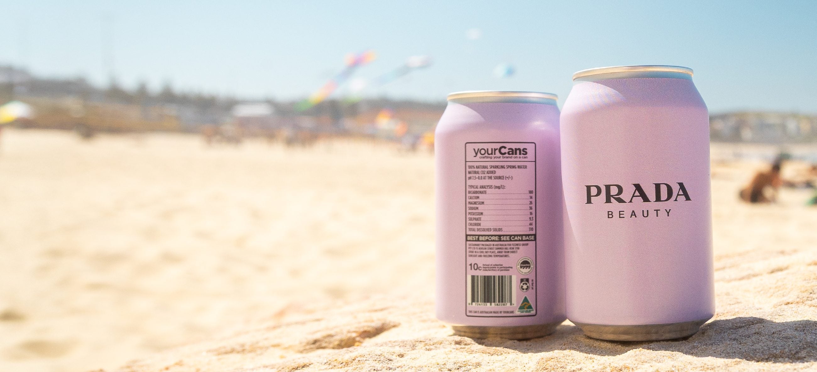 Prada Beauty branded cans on the sand